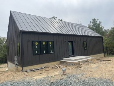 Dark-clad barn-style new construction home with standing-seam metal roof and matching dark gutters