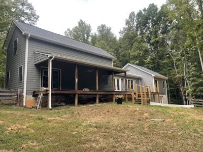 Gray rural ranch home in a wooded lot with new gutters and a covered back porch