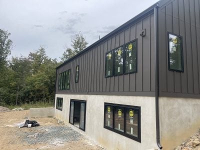 Modern board-and-batten home with dark-bronze metal roof and new black gutters under construction